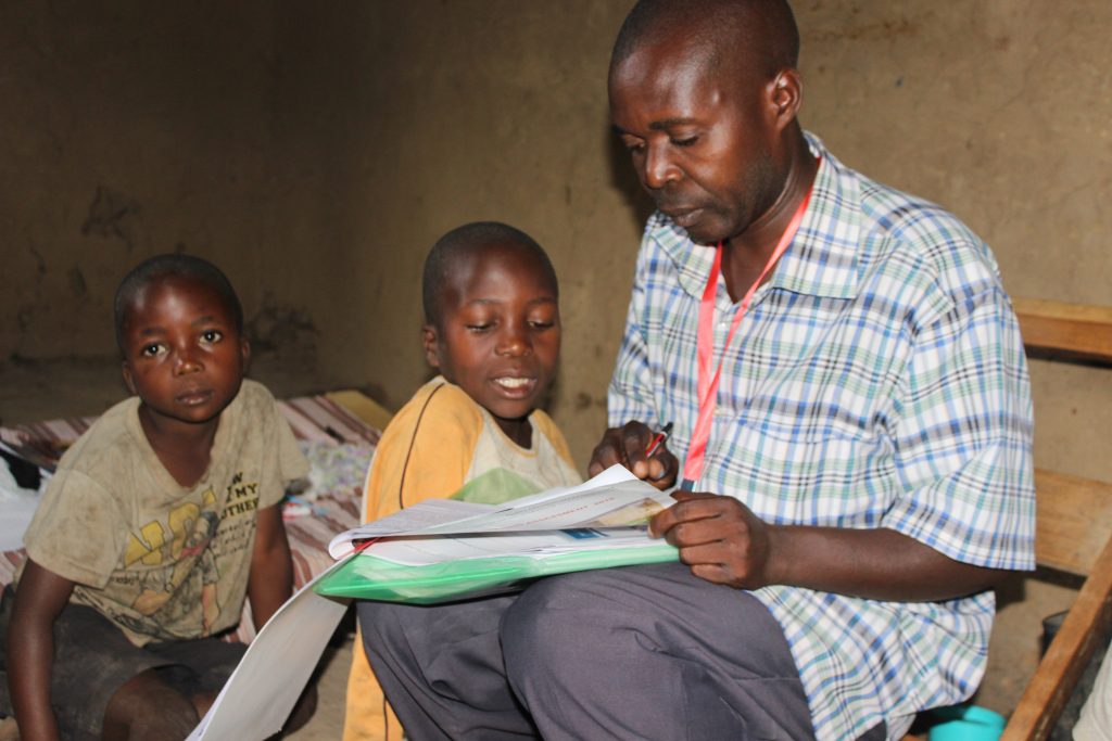 A-parent-helps-his-children-to-go-through-some-of-the-study-kits-recieved-from-ECW-implementing-partners-in-Uganda--1024x683